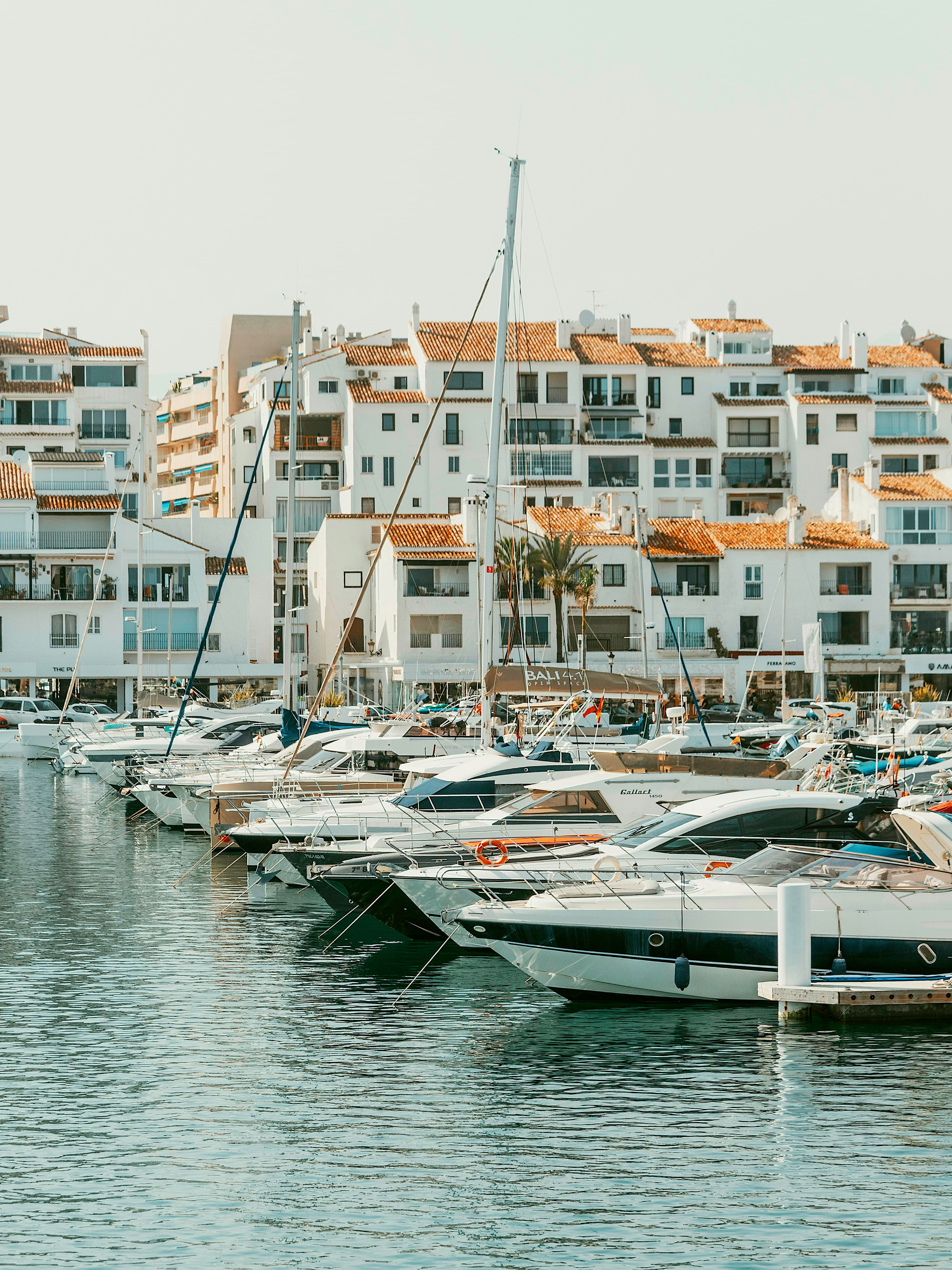 Sailboats and yachts moored at Puerto Banús marina with white buildings behind